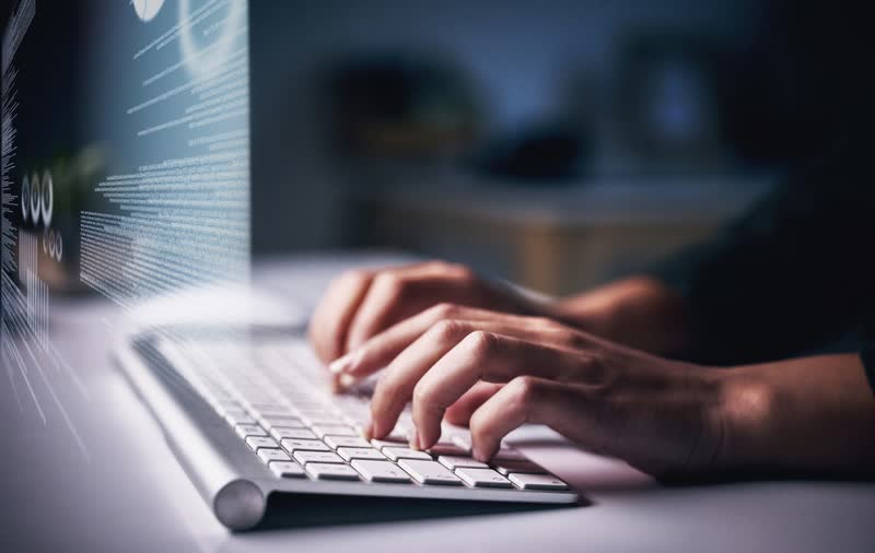 Des mains sur un clavier d'ordinateur, devant un écran de code