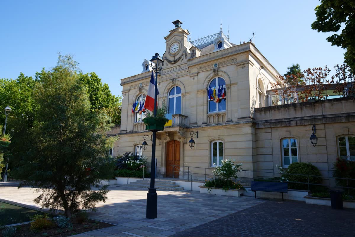 Façade d'une mairie sous un ciel bleu, avec des drapeaux aux fenêtres