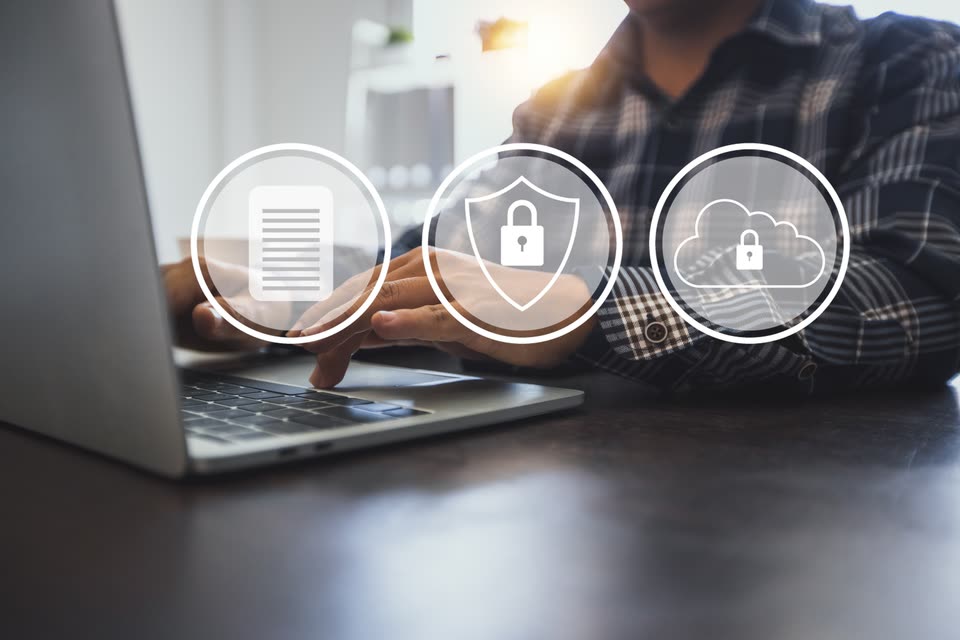 Une personne au clavier d'un ordinateur portable, devant trois pictogrammes : un document, un bouclier avec un cadenas et un nuage avec un cadenas