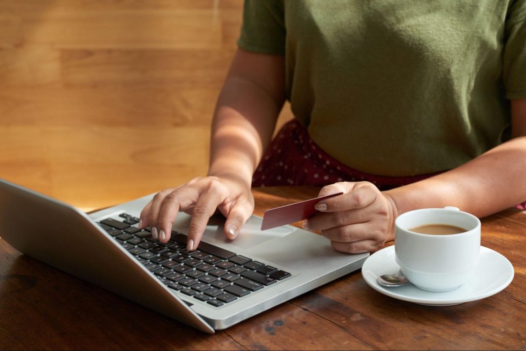 Personne utilisant un ordinateur portable avec une carte bancaire à la main et une tasse de café à proximité.